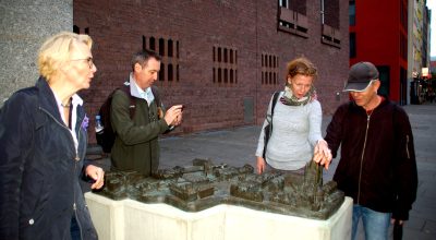 Przewodniczka i zwiedzający przy odlanej w brązie makiecie Starego Ratusza i jego okolic w Kolonii, w Nadrenii - fot. Cezary Rudziński