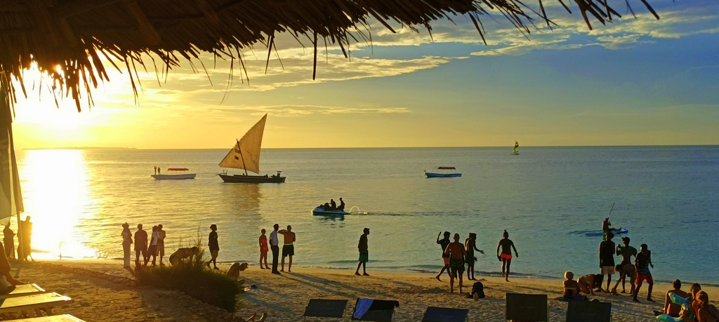 Wybrzeże Zanzibaru. Widok na ocean, łódź żaglową i ludzi na brzegu.